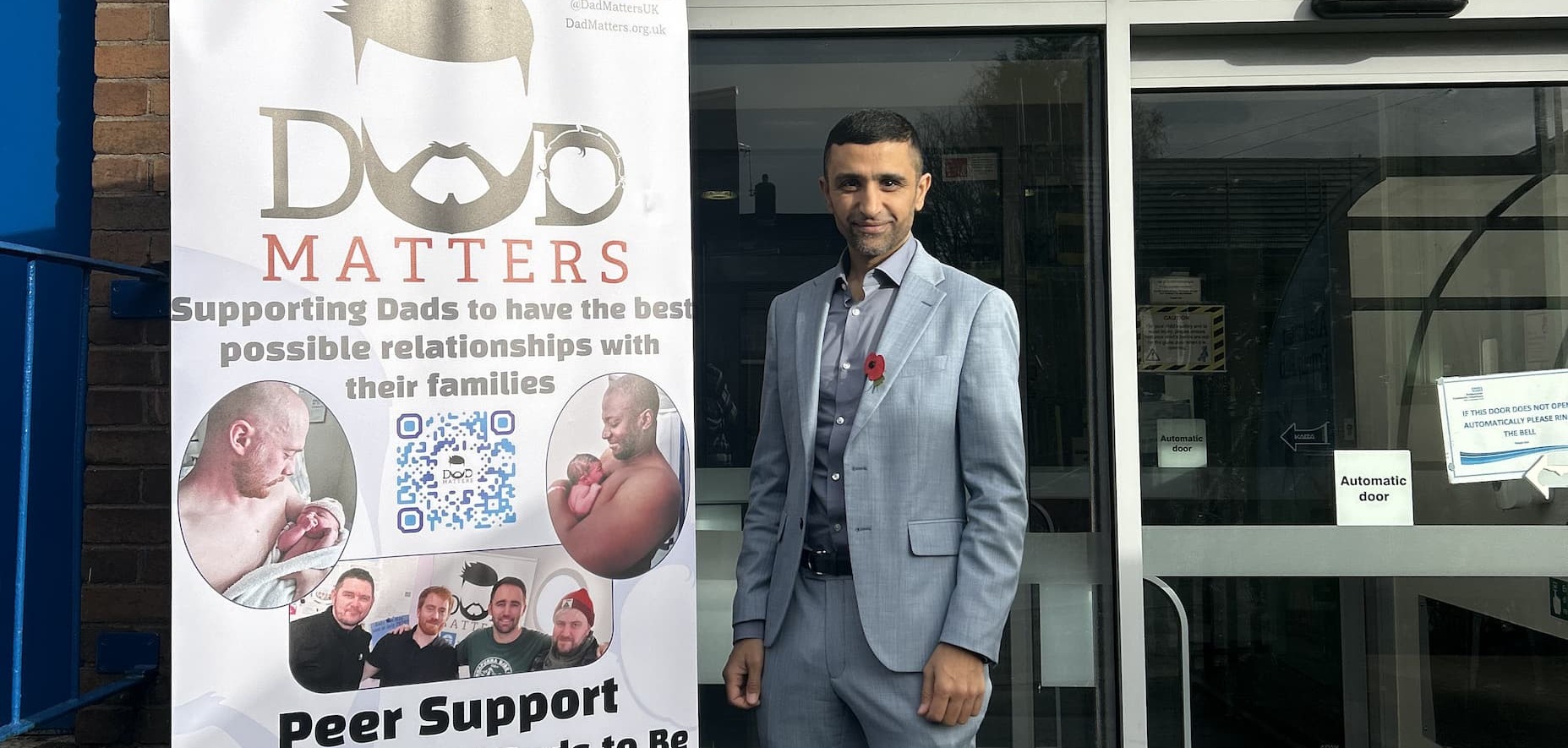 Cllr Shaid Mushtaq standing outside Alexandra Family Hub next to a 'Dad Matters' sign 