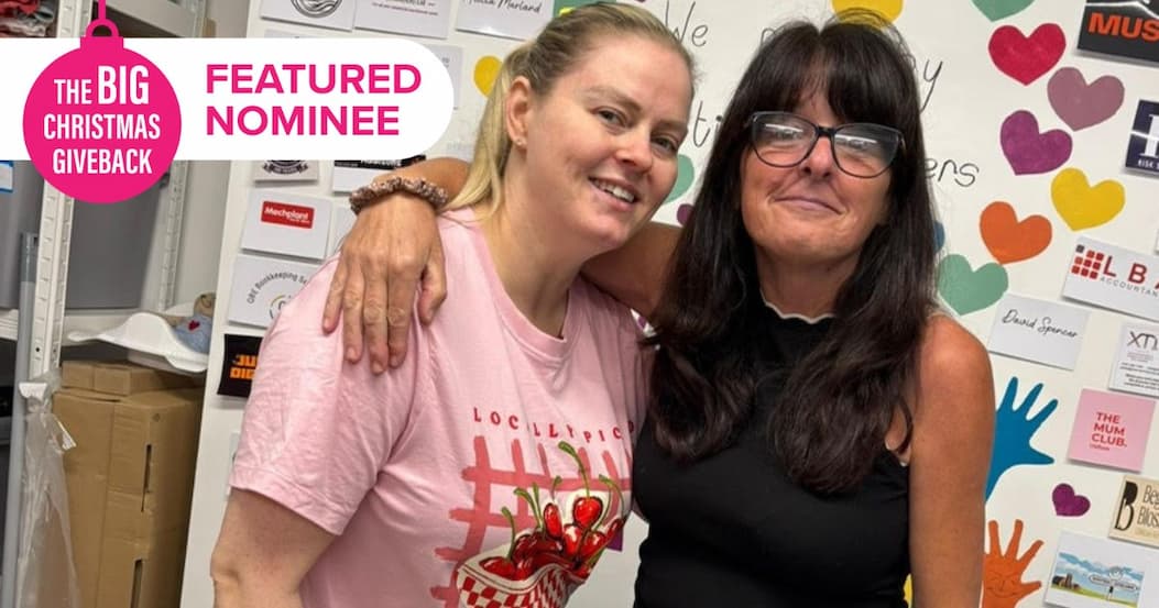 Our Community Wardrobe founder Sally Maher (right) smiling next to fellow director Laura Washington in front of a colourful display