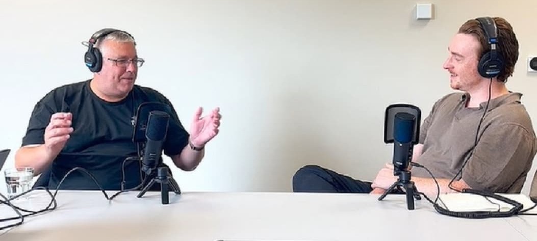 Pub landlord Chris Riley gesturing with his hands and smiling wearing headphones as he chats with podcast presenter Robin Marshall who is also smiling 