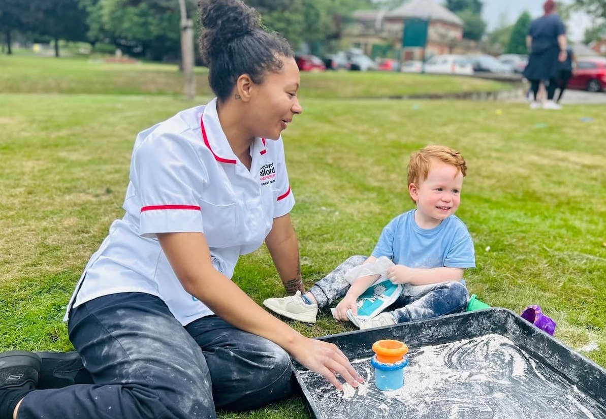 A woman and child smiling as they enjoy a messy play activity in the park