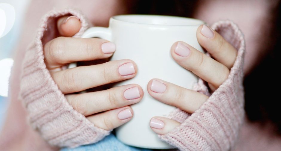 A person wearing a warm jumper over their hands to keep warm holding a hot drink in a mug