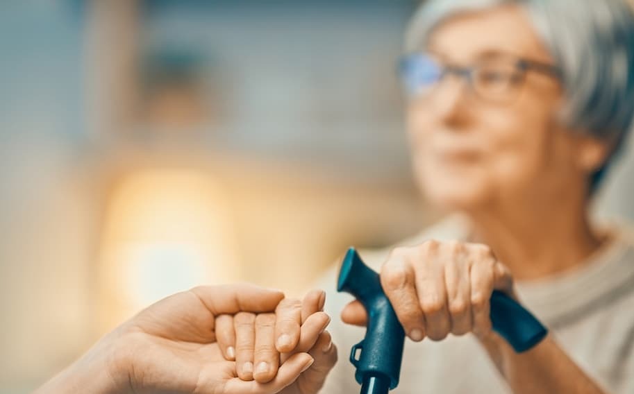 An adult holding the hand of a senior woman