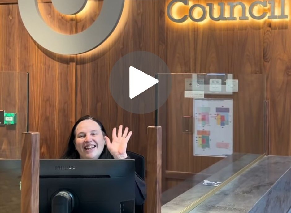 Receptionist Lynn waving from behind the welcome desk at the J.R Clynes building