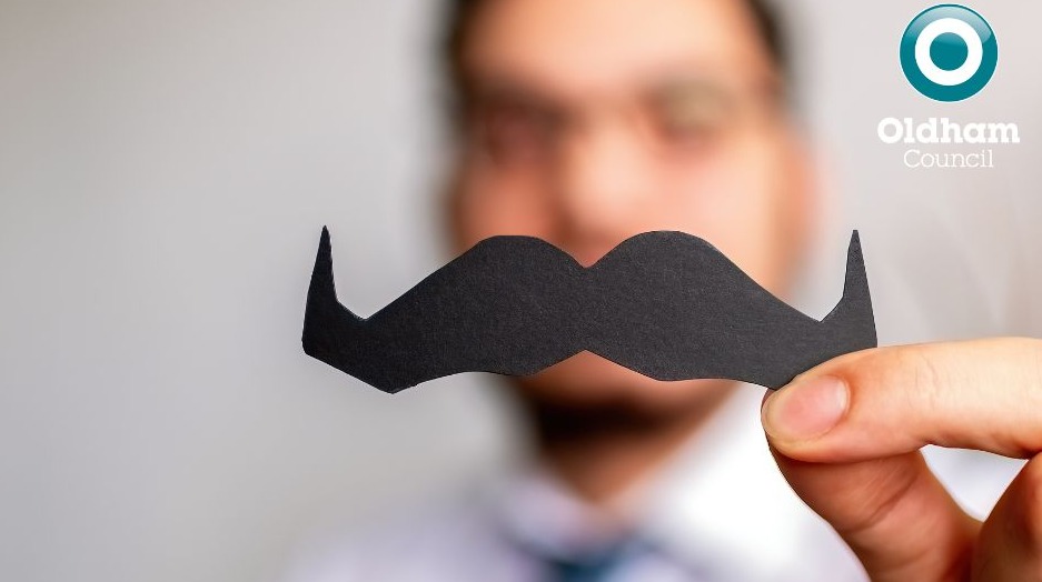 A man holding a paper cut-out moustache 