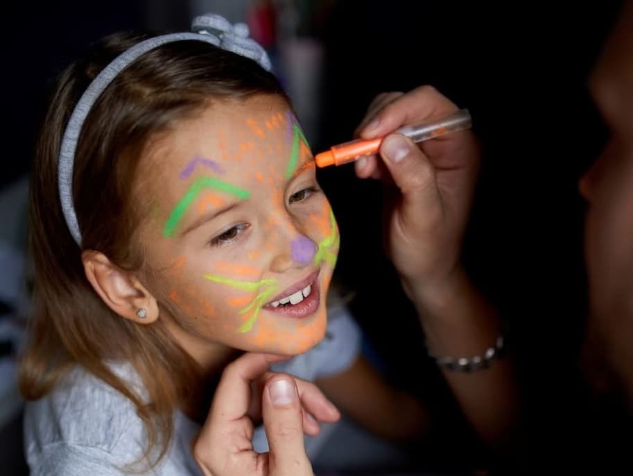 A smiling little girl having her face painted in luminous colours