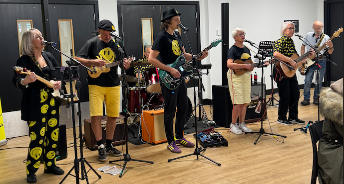 Musicians from the band The Happy Hours performing at The Loom in yellow smiley face patterned outfits