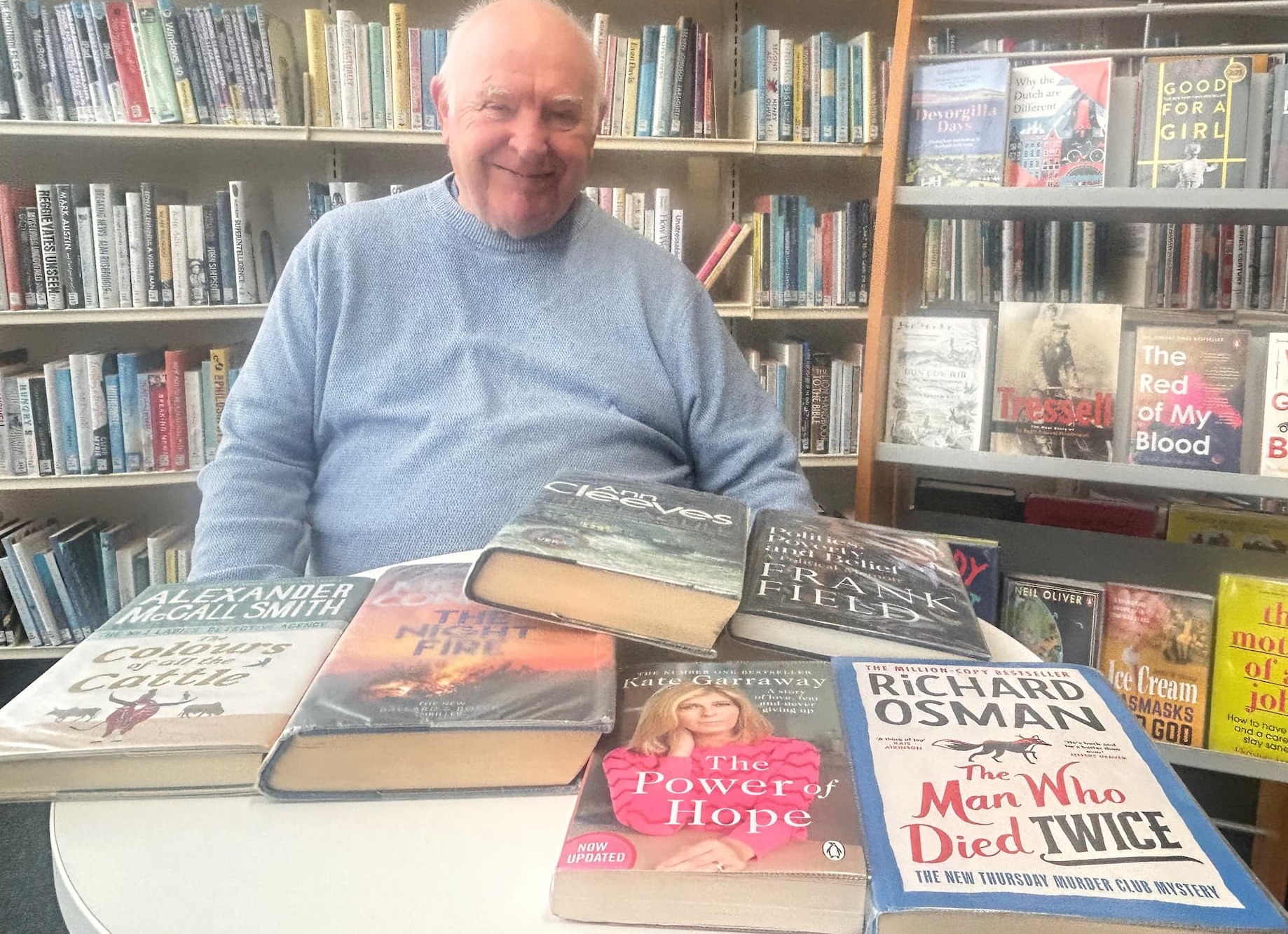 Cllr Peter Dean seated in Oldham Library smiling with an assortment of books 
