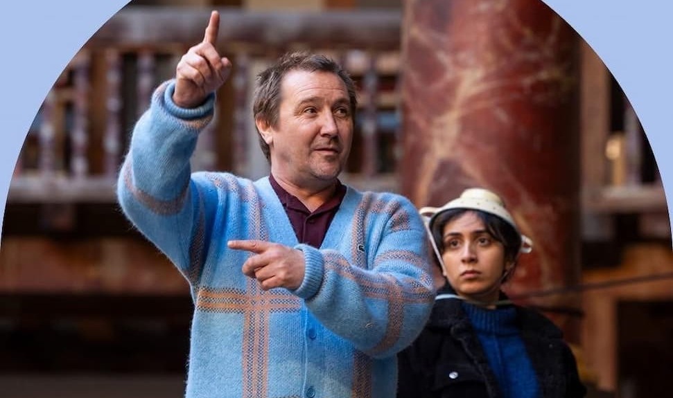 New Creative Director Nick Bagnall pointing wearing blue tartan patterned cardigan as a person looks on