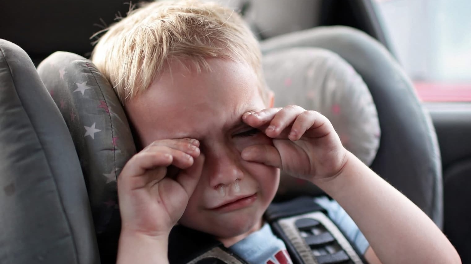 Young upset child holding their hands over their eyes as they cry in a car child seat
