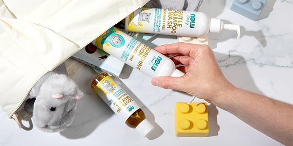 Hand reaching into a bag pulling out NOW Baby Nourishing Lotion, Soothing Baby Oil and Gentle Shampoo & Wash 