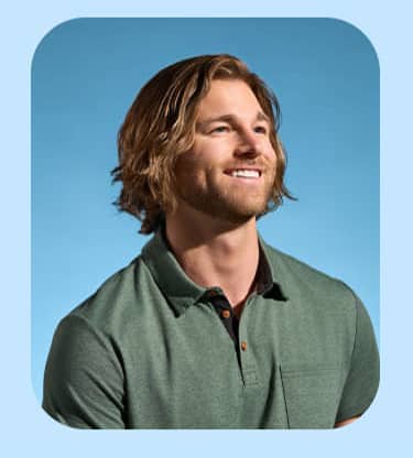 A blond man with a beard in a green shirt smiles toward the sun.