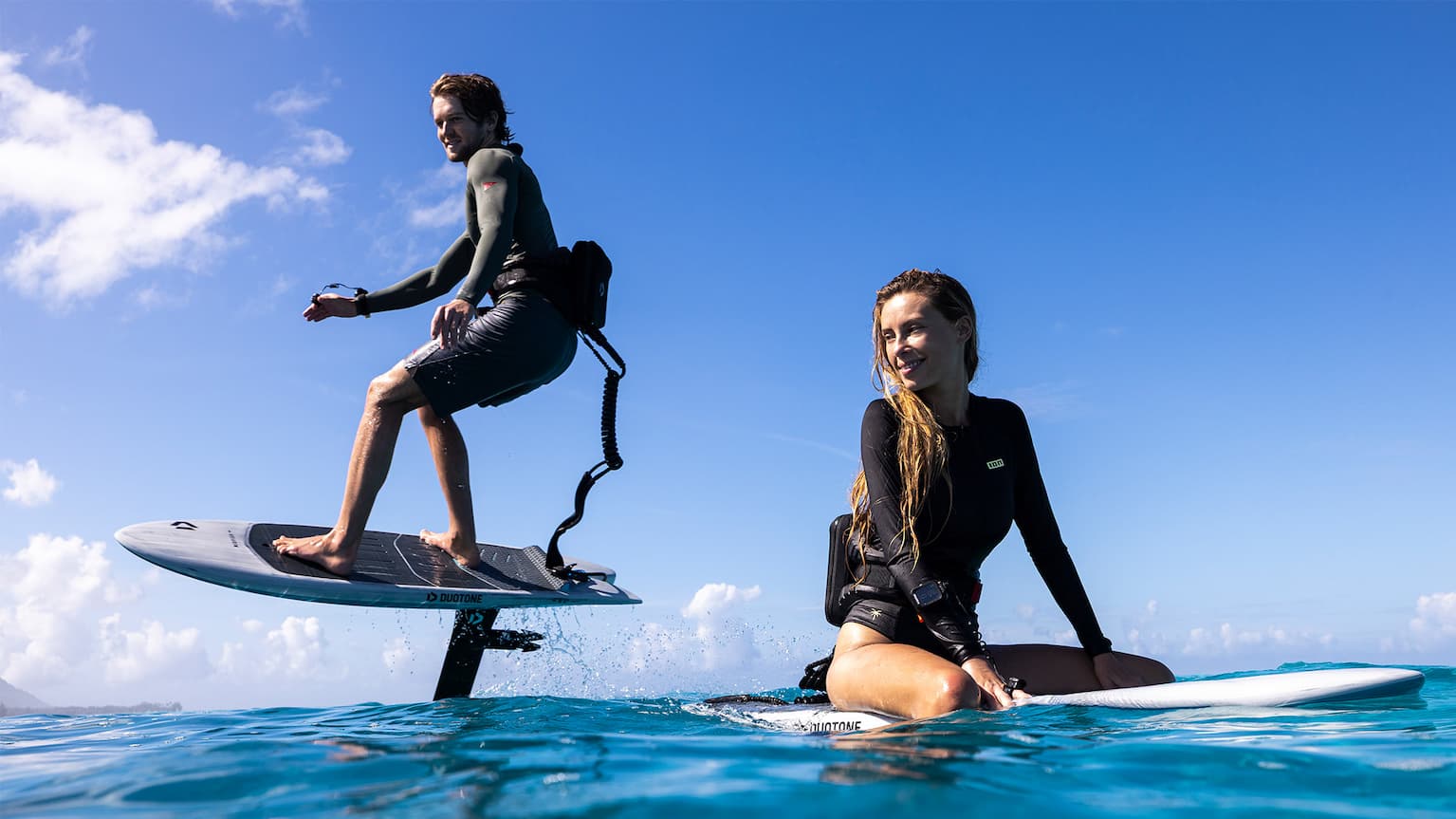an image of a woman sitting on the Midfish and a man foiling with the Foil Assist around her
