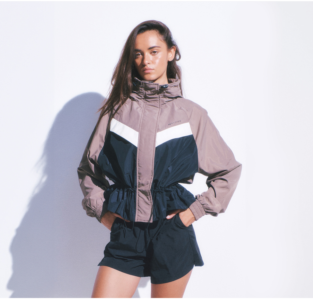 Studio shot of a brunette woman wearing a P.E Nation spray jacket and active shorts.