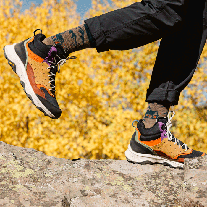 Shop Hike Hike Hut sock - a hiker wears earth-toned socks with mountain and cabin designs