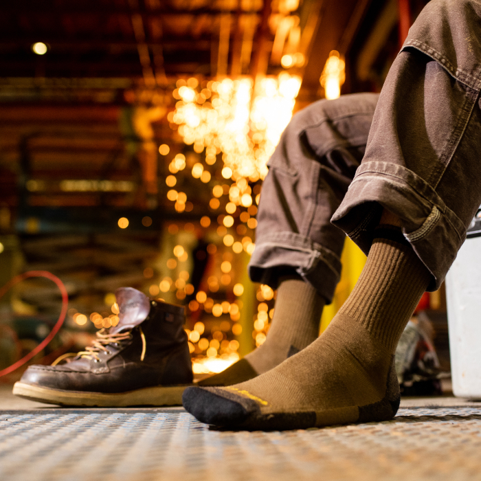 Shop wool work socks - a pair of feet wearing olive work socks in a factory with sparks flying in the background