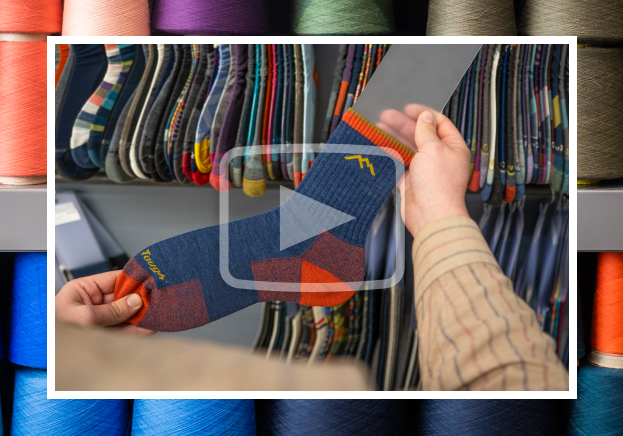 Watch the Video - a worker inspects a 1466 sock, hanging on a rack of samples