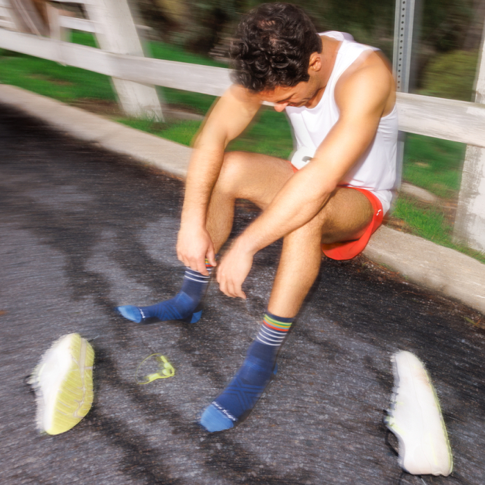 Darn It - an exhausted runner sits on the side of the road wearing blue Darn Tough socks