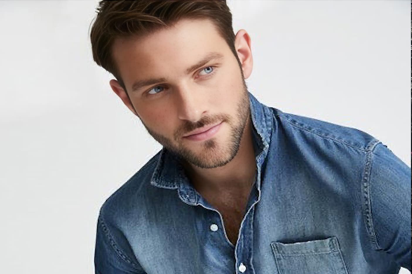Close-up portrait of a man wearing a faded blue denim button-down shirt against a white background. Fearrington Village.