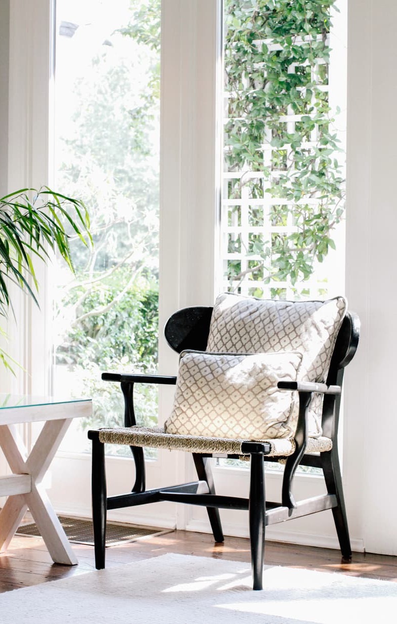Sunlit seating area with a black woven chair, patterned cushions, and garden views at The Fearrington House Inn. Fearrington Village.