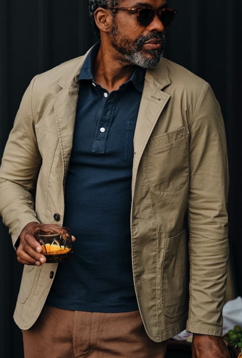 Man wearing a lightweight tan blazer over a navy polo with brown trousers and sunglasses. Fearrington Village.