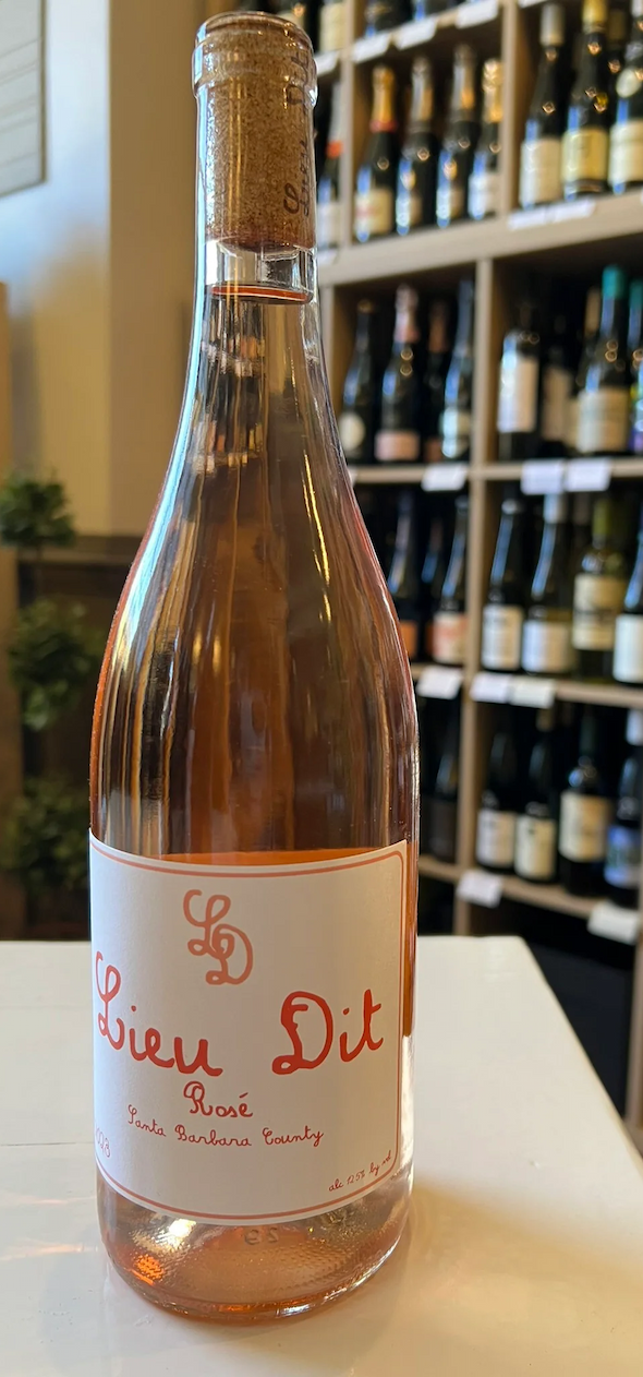 A bottle of Lieu Dit Rosé from Santa Barbara County displayed on a white counter in front of softly blurred wine shelves. The pale rosé and minimalist label create a fresh, elegant wine shop presentation.