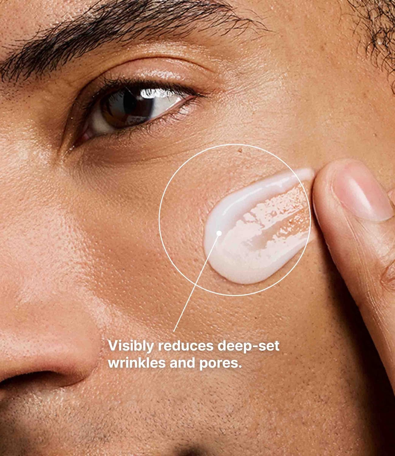 Close-up of a person's cheek and eye area as a fingertip applies a smooth layer of skincare cream to the skin. A graphic callout highlights the application area, accompanied by text stating, “Visibly reduces deep-set wrinkles and pores,” emphasizing the product’s anti-aging and skin-smoothing benefits.