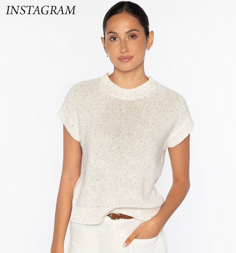 Woman wearing a short-sleeve cream knit top paired with light trousers, standing against a neutral background.