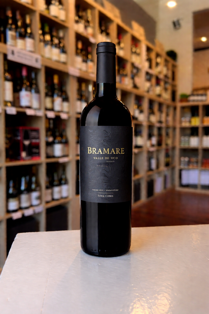 Bottle of Bramare Valle de Uco Malbec standing on a counter in a wine shop, with shelves of wines softly blurred in the background.