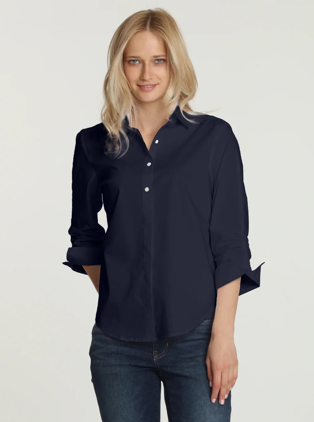 A woman with blonde hair wears a navy button-down shirt and jeans, standing against a plain light background.
