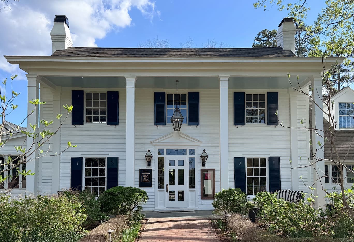 Front exterior of the Fearrington House Restaurant with white columns, black shutters, and a brick walkway leading to the entrance. Fearrington Village.