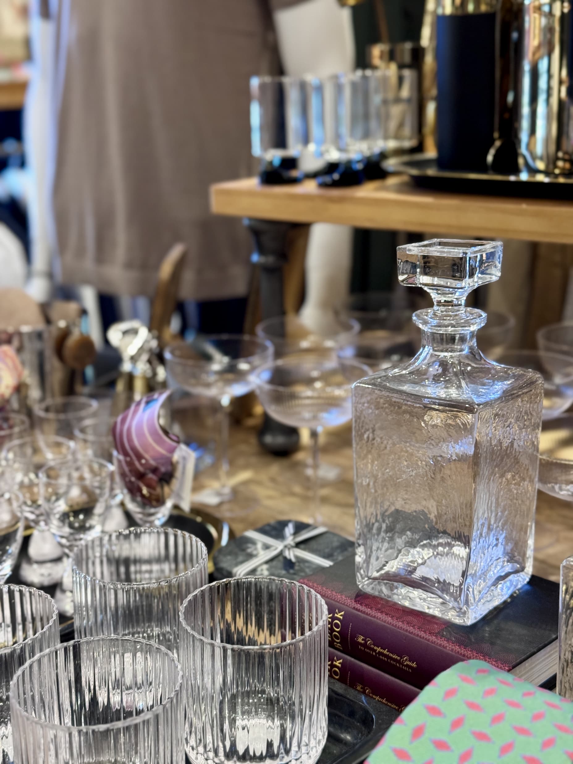 Display of glass decanters, cocktail glasses, and barware arranged on a tabletop inside a home and gift shop. Fearrington Village.