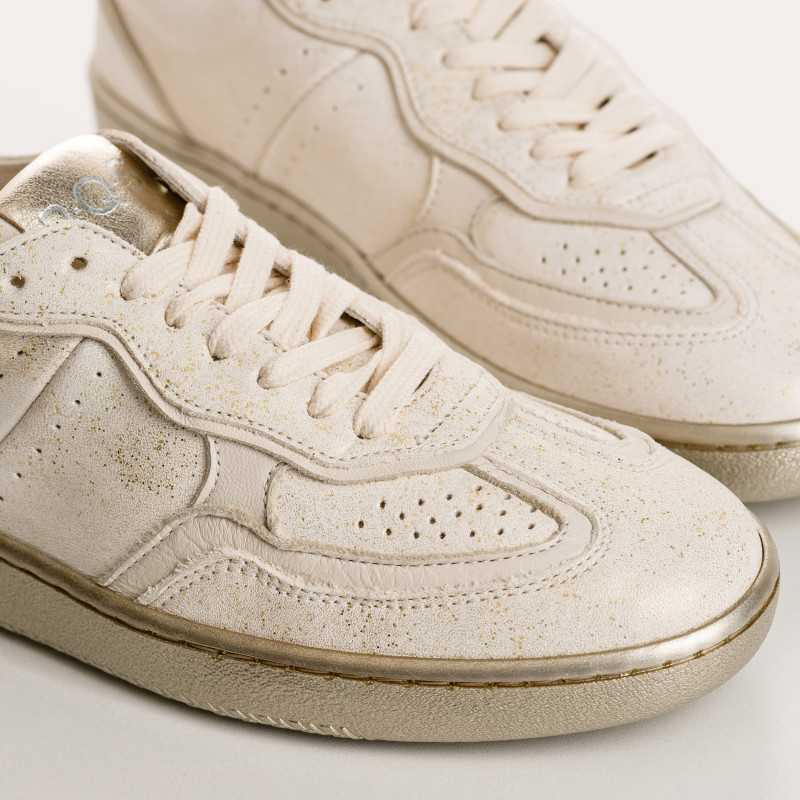 Close-up of white leather lace-up sneakers with perforated detailing and slightly textured soles, shown from an angled side view.