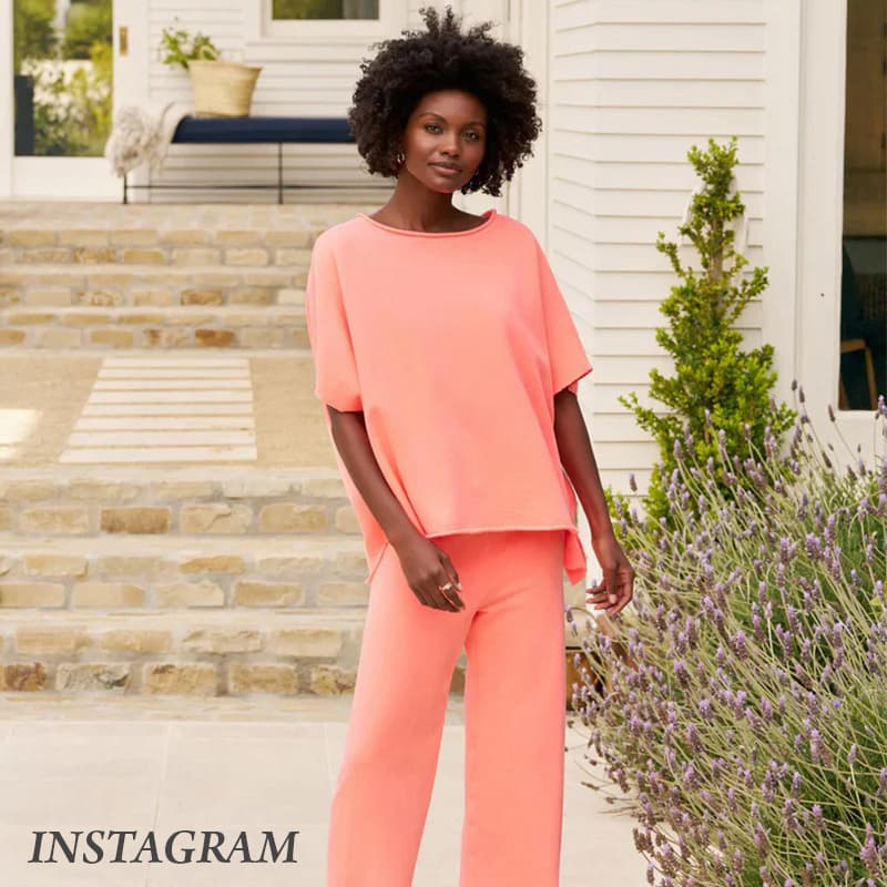 Woman wearing a coral lounge set outside a white cottage surrounded by blooming lavender. Fearrington Village.