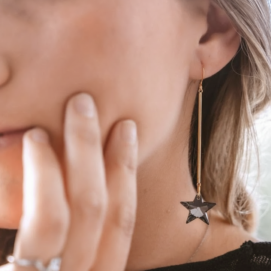 Close-up of a woman's ear with a dangling gold earring featuring a dark star charm.