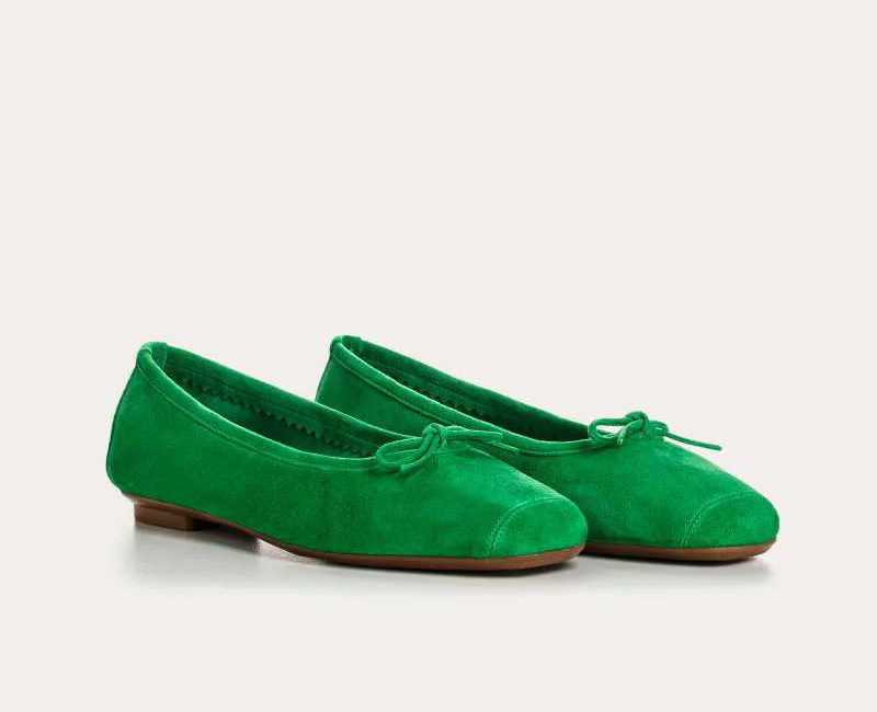 Pair of green suede ballet flats with small bow ties at the toes and low brown soles, shown on a light neutral background.
