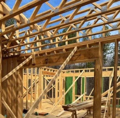 Wood framing of a building under construction, showing exposed beams, roof trusses, and support braces against a blue sky.