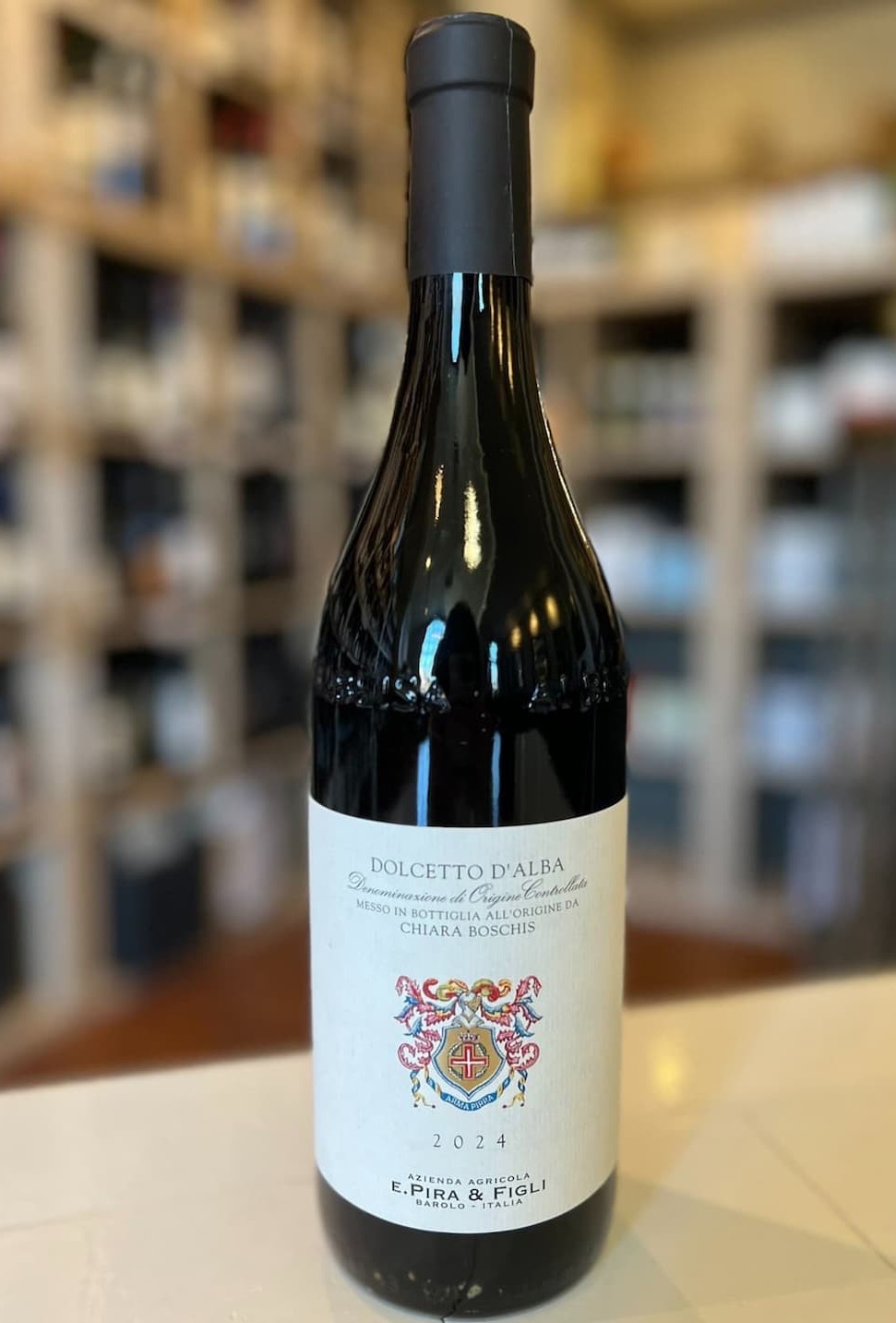 Bottle of Dolcetto d’Alba 2024 by E. Pira & Figli (Chiara Boschis), shown on a counter with a softly blurred wine shop background.