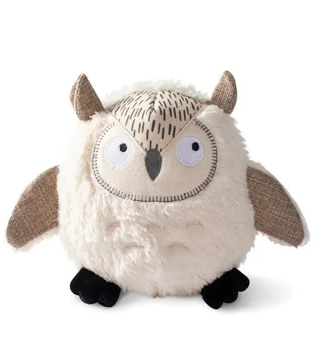 A round, plush owl toy with beige fur, fabric wings and ears, large stitched eyes, a small beak, and soft black feet. Fearrington Village