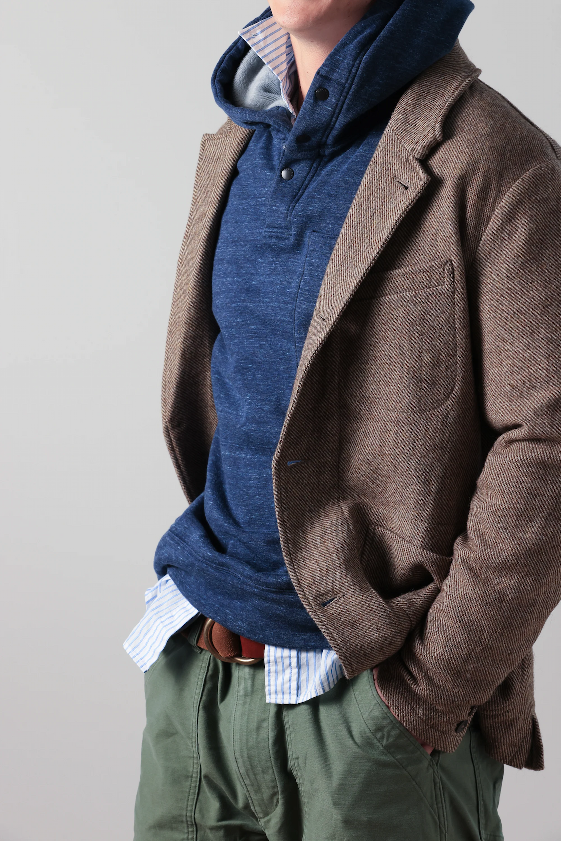 Man layering a brown textured blazer over a blue hooded pullover and striped shirt with green trousers. Fearrington Village.