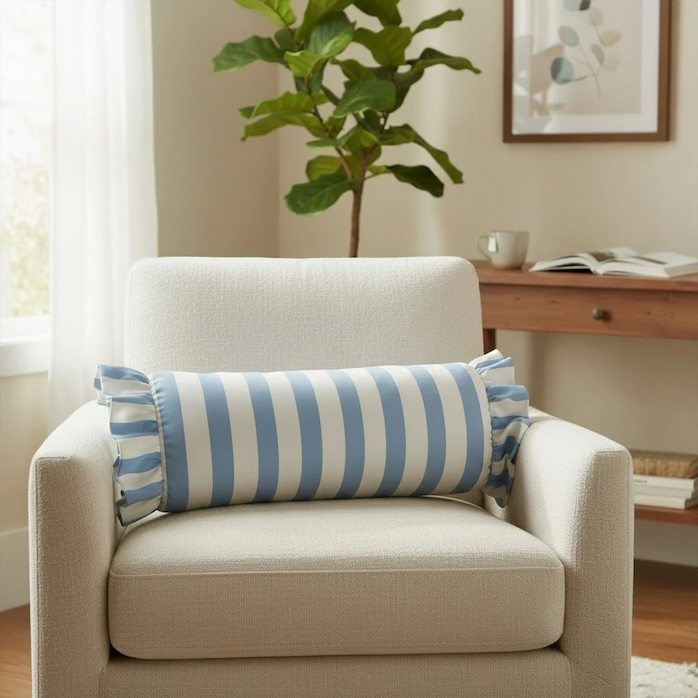Blue and white striped bolster pillow with decorative ruffled ends displayed on a white armchair. Fearrington Village.