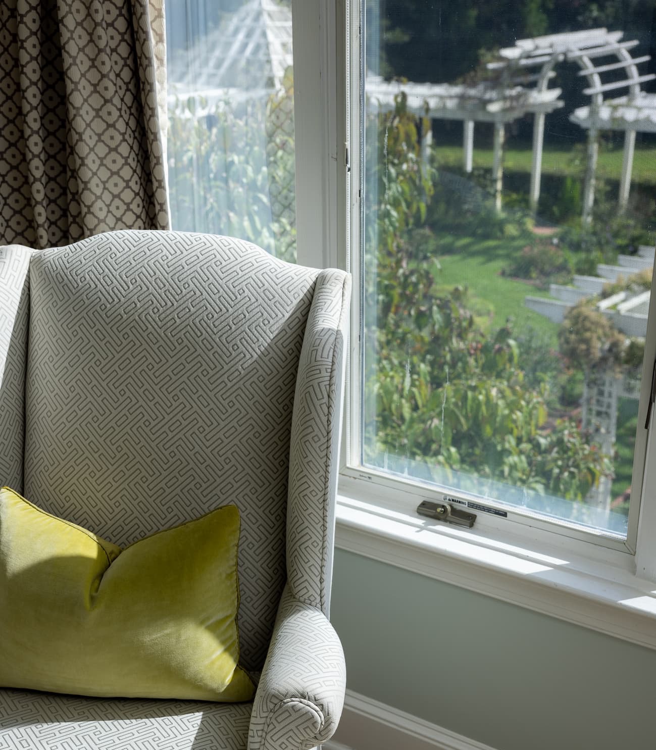 Cozy guest room reading chair beside a sunlit window overlooking the gardens. Fearrington Village.