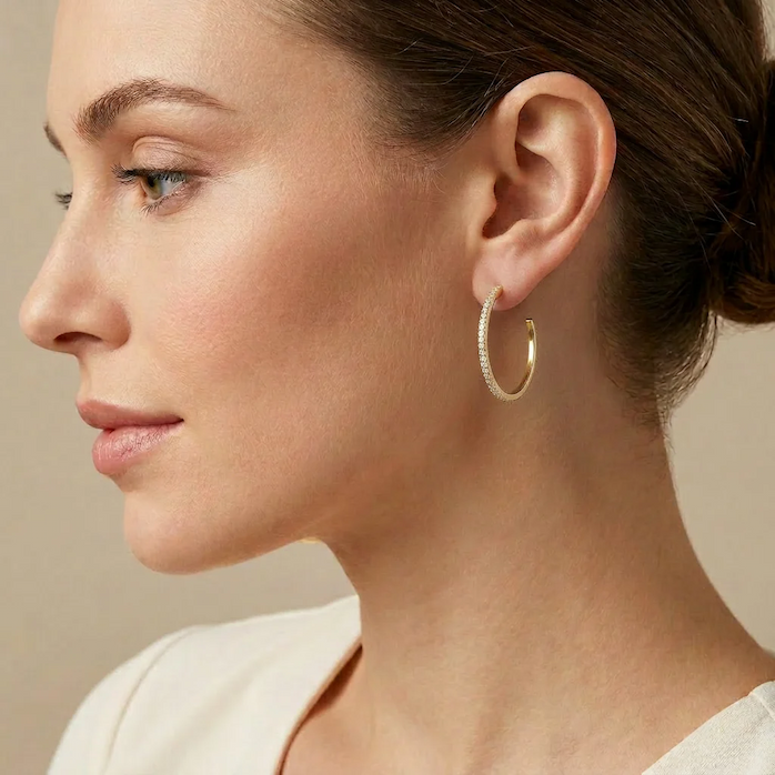 Side-profile close-up of a woman wearing a slender gold hoop earring accented with pavé diamonds, showcasing the earring’s refined sparkle and timeless elegance against a soft neutral backdrop.