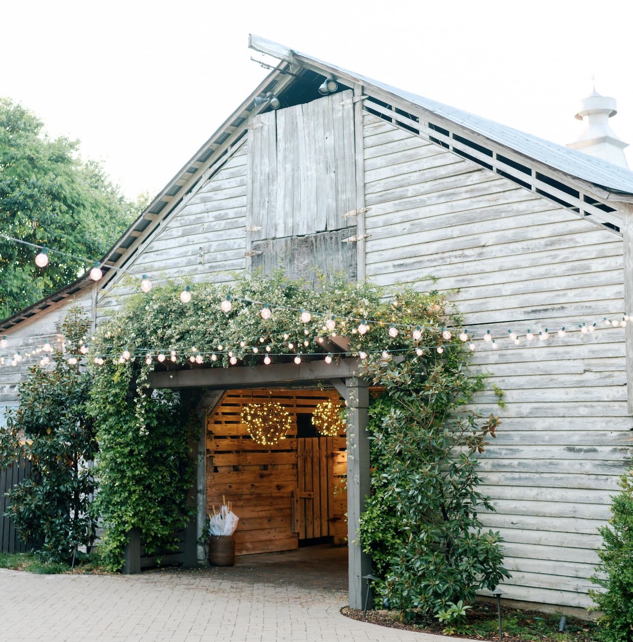Rustic white barn with string lights, greenery framing the entrance, and warm decorative lighting inside. Fearrington Village.