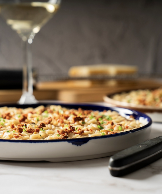 Creamy risotto topped with savory crumbles and fresh herbs, served alongside a glass of white wine. Fearrington Village.