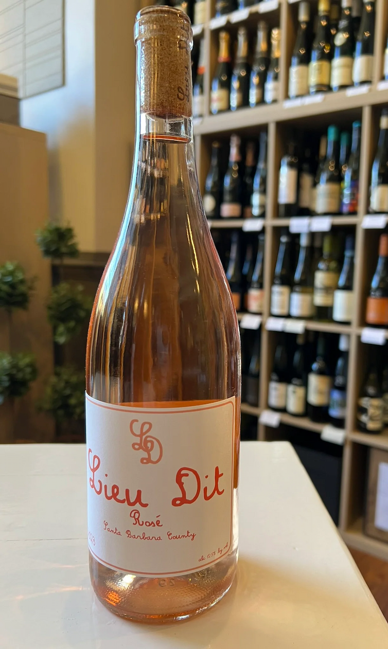 A bottle of Lieu Dit Rosé from Santa Barbara County displayed on a white counter in front of softly blurred wine shelves. The pale rosé and minimalist label create a fresh, elegant wine shop presentation.