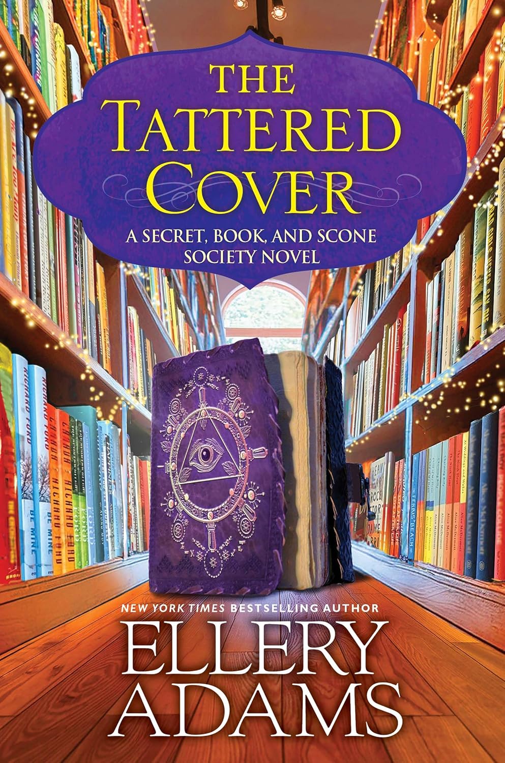 Book cover for "The Tattered Cover" by Ellery Adams, featuring shelves of colorful books, a glowing background, and a purple book with an intricate mystical design and an eye on the front, placed in the foreground. Fearrington Village
