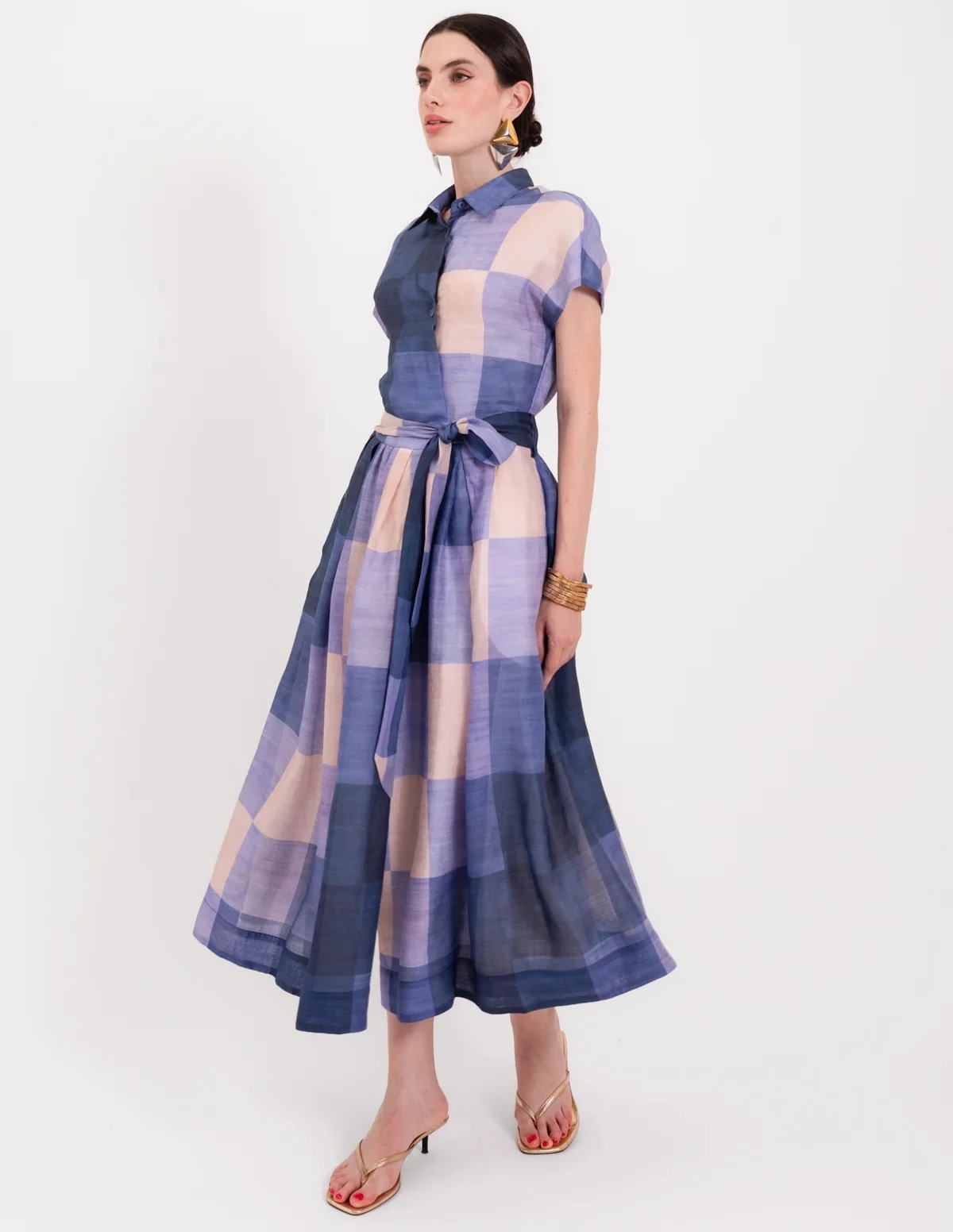 Woman wearing a blue and blush plaid belted midi dress with statement earrings and gold accessories. Fearrington Village.