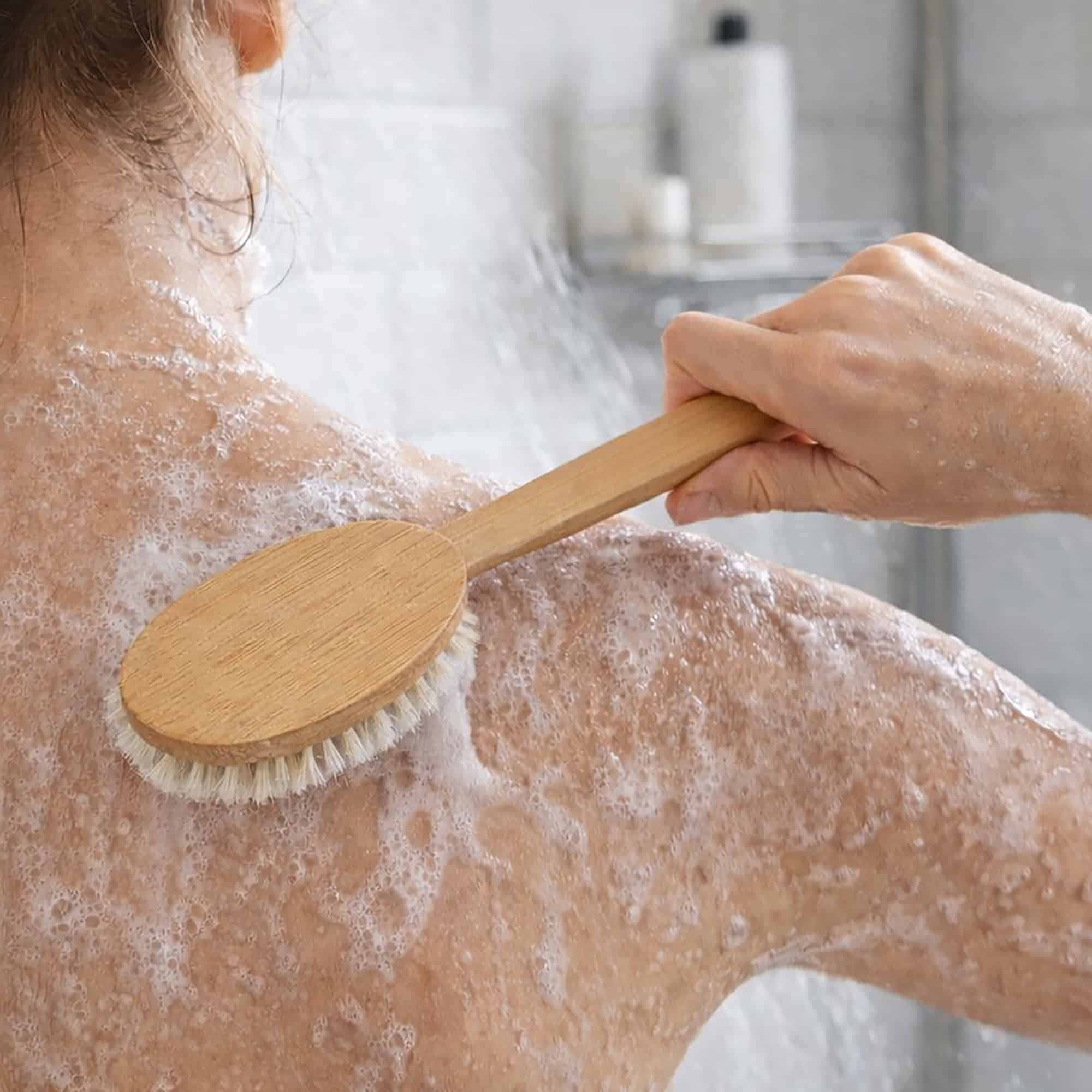 Person using a long-handled body brush to cleanse and exfoliate their back in the shower. Fearrington Village.