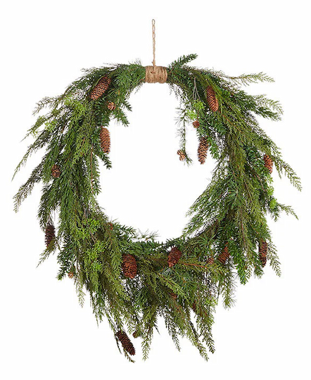 A wreath made of green pine branches and brown pinecones hangs from a loop of twine. The arrangement is natural and slightly asymmetrical, giving it a rustic and festive appearance. Fearrington Village