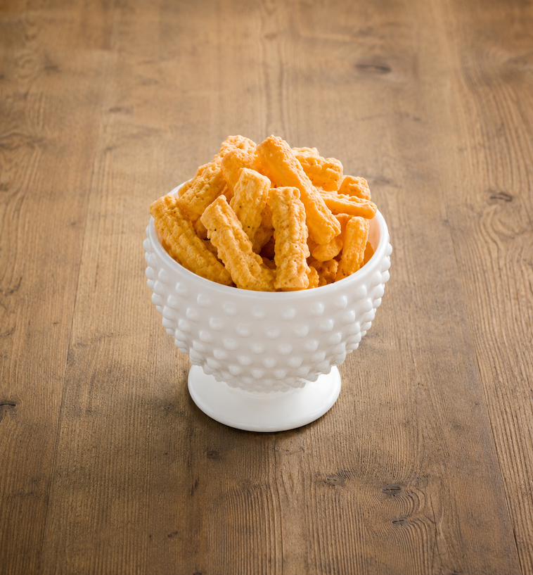 Bowl of crunchy cheese straws served in a white hobnail pedestal bowl on a rustic wooden table. Fearrington Village.